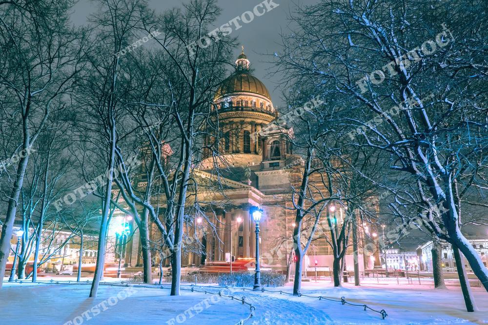 На фотографии изображен Исаакиевский собор в зимнюю ночь. Снежный парк и голые деревья создают атмосферу спокойствия и уюта, а мягкая подсветка подчеркивает величие архитектурного памятника. Золотой купол собора выделяется на фоне темного неба, добавляя снимку торжественности. Исаакиевский собор – один из символов Санкт-Петербурга и его исторического наследия.